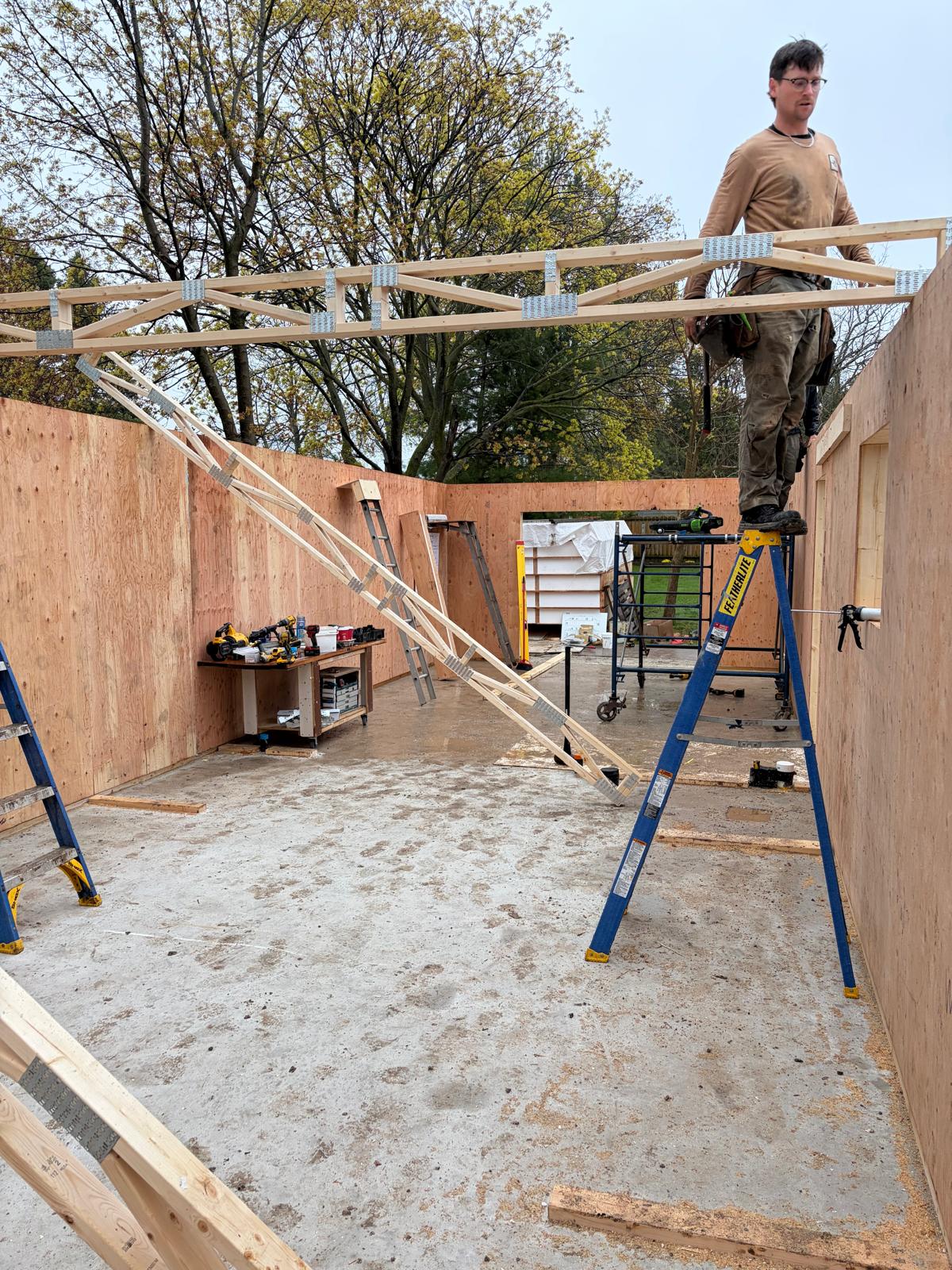 Interior view looking up at roof trusses being installed on SIP panel home with worker on top