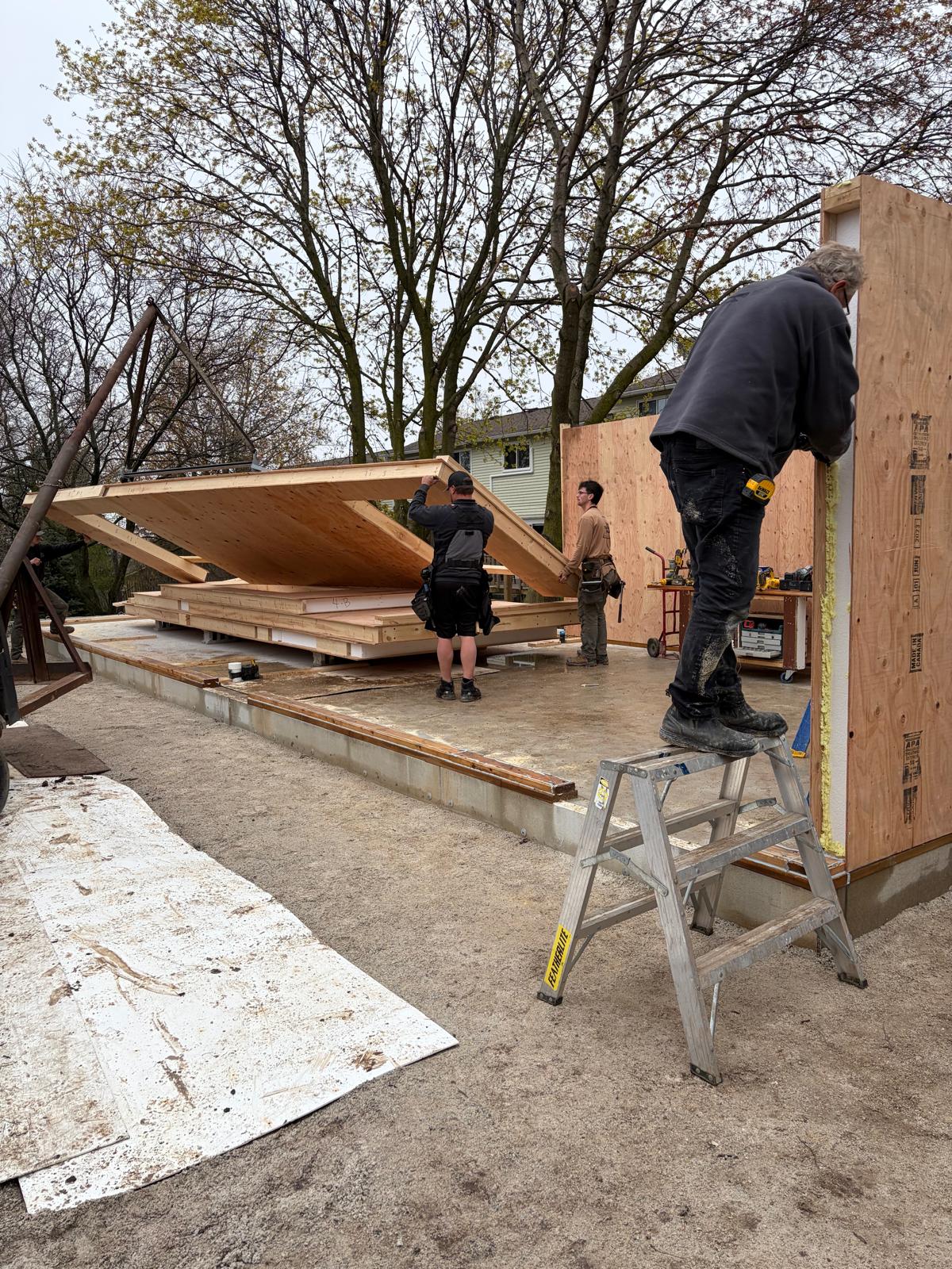 Construction workers raising and positioning large SIP wall panels together on build site